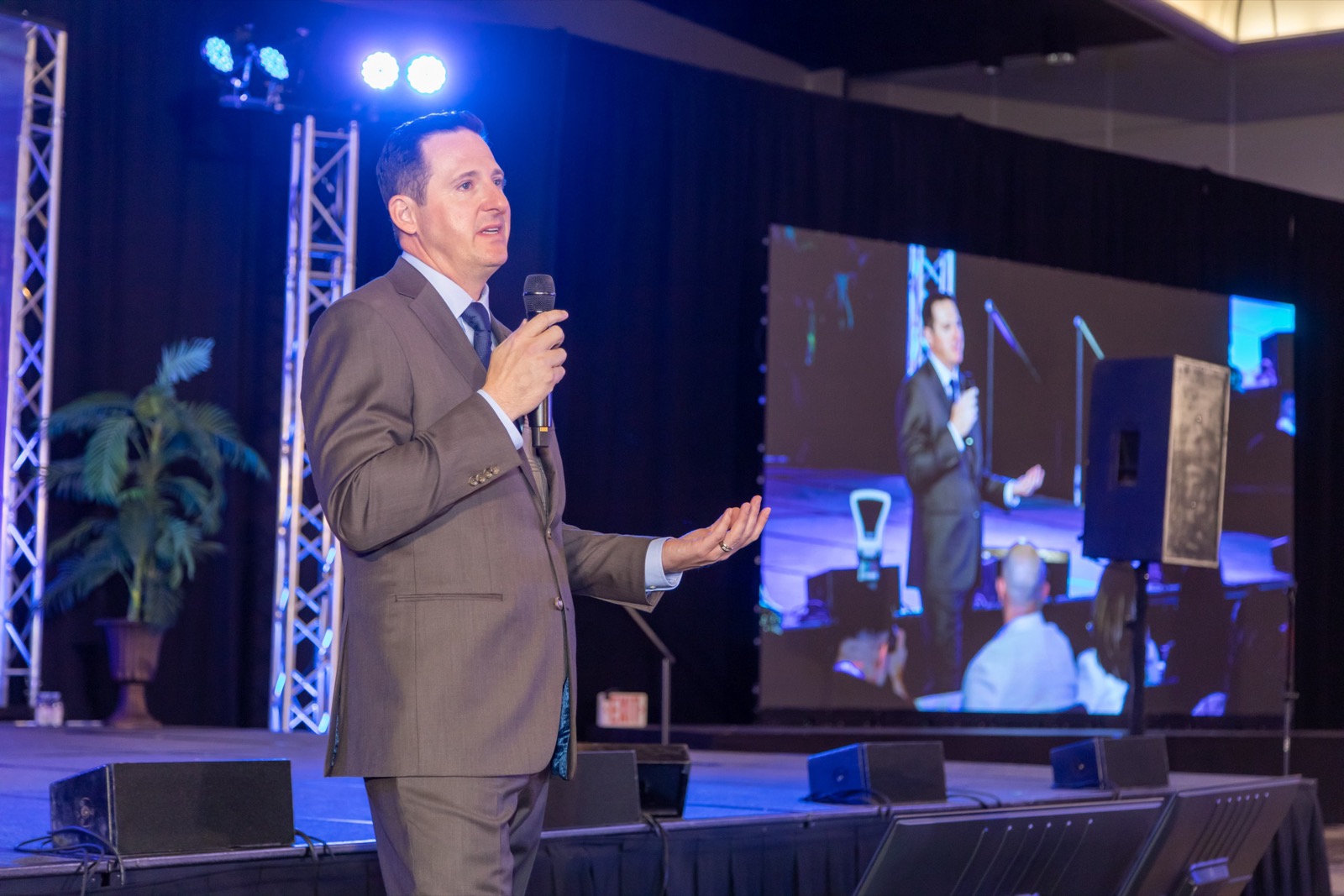 A conference speaker on stage next to his live IMAG feed
