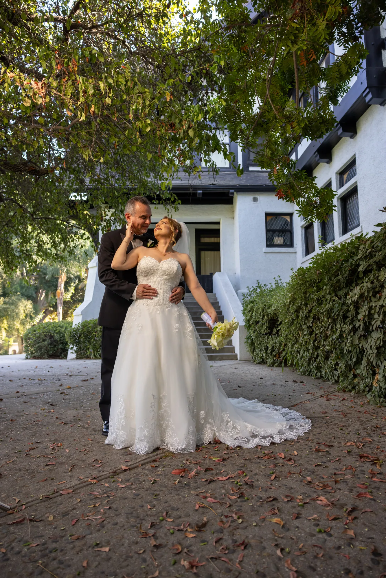 Bride and groom under the tree canopy beside a historic house at Ambassador Mansion & Gardens