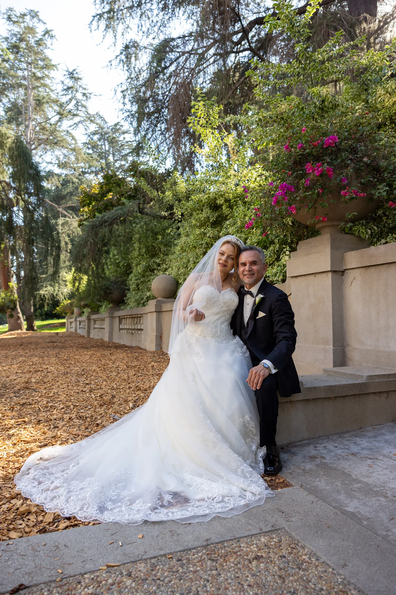 Bride seated on the stone balustrade with bougainvillea behind at Ambassador Gardens