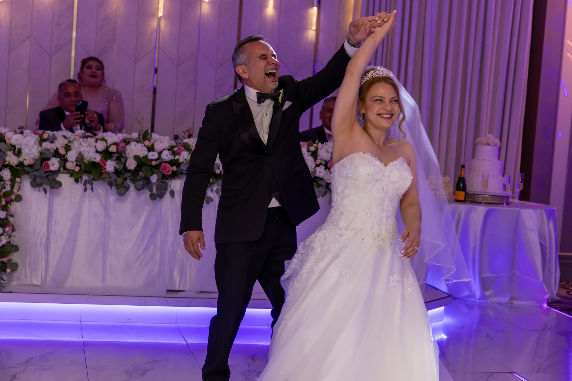 Bride and groom entering the ballroom under magenta uplighting at De Luxe Banquet Hall