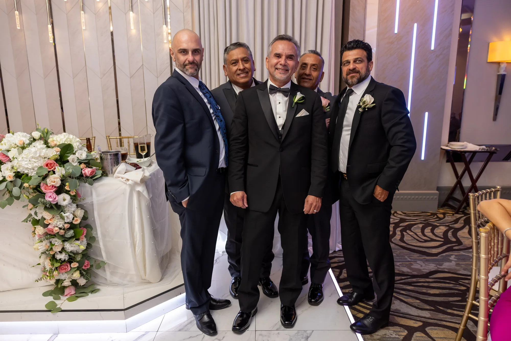 Groomsmen beside the floral backdrop and light bars at De Luxe Banquet Hall, Burbank