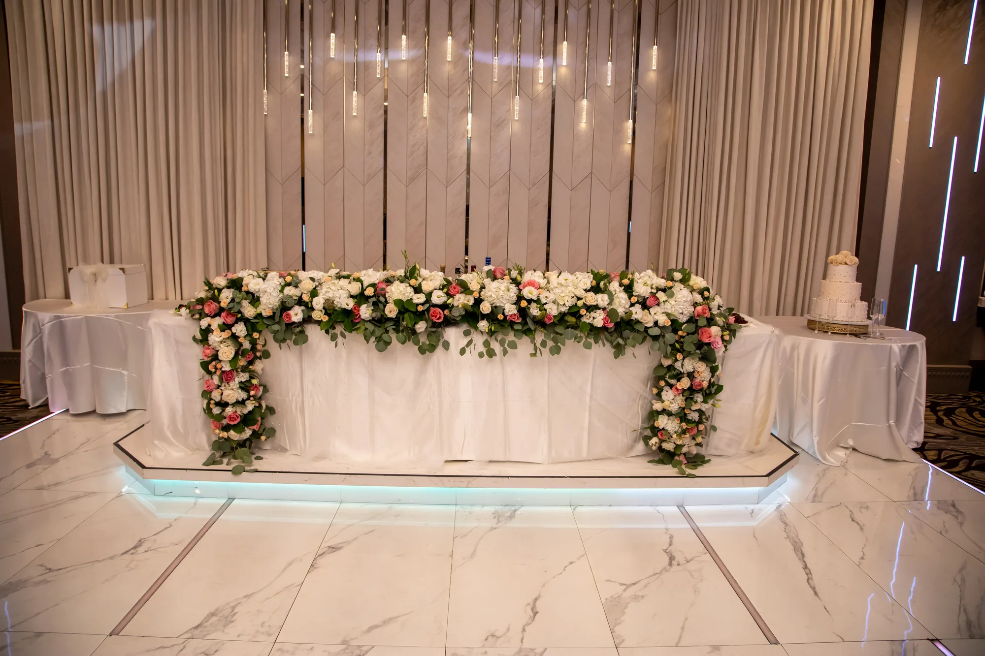 Sweetheart table with florals on a lit marble plinth at De Luxe Banquet Hall