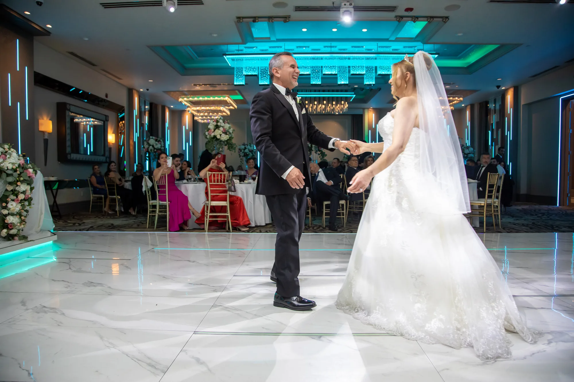 Wide view of the reflective marble dance floor under teal lighting at De Luxe Banquet Hall